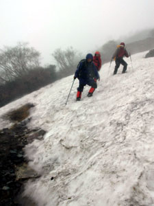 残雪で覆われた登山道。急傾斜の雪上をアイゼンやピッケルを使って慎重に足を進める登山者