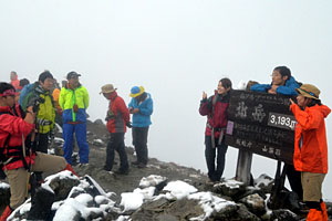 ７日に初冠雪を観測した北岳山頂。霧の中を登頂し、記念撮影をする登山者も目立った