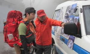 写真で山頂付近の雪の様子を確認する登山客（左）＝南アルプス市芦安芦倉