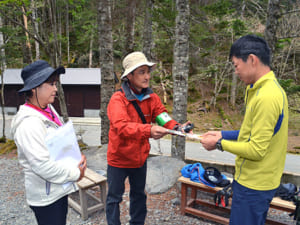 長野県側から訪れた登山者（右）に啓発チラシを手渡す芦安ファンクラブのメンバー＝南アルプス・北沢峠